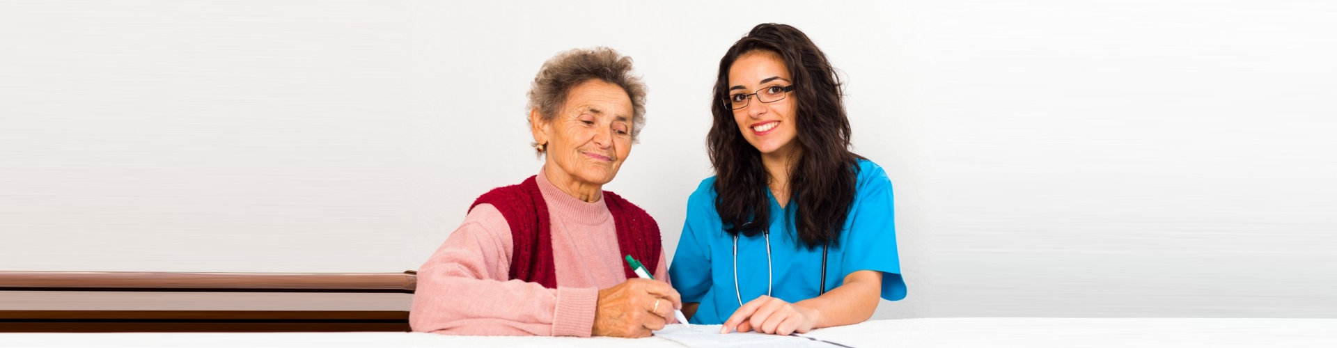 elder woman filling out forms with assistance by a caregiver